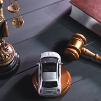 A scale of justice, gavel, and a toy car on a wooden table, suggesting legal themes.