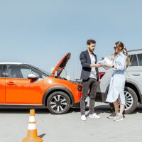 Man and woman arguing, standing together on the road with their cars on the background after the car accident